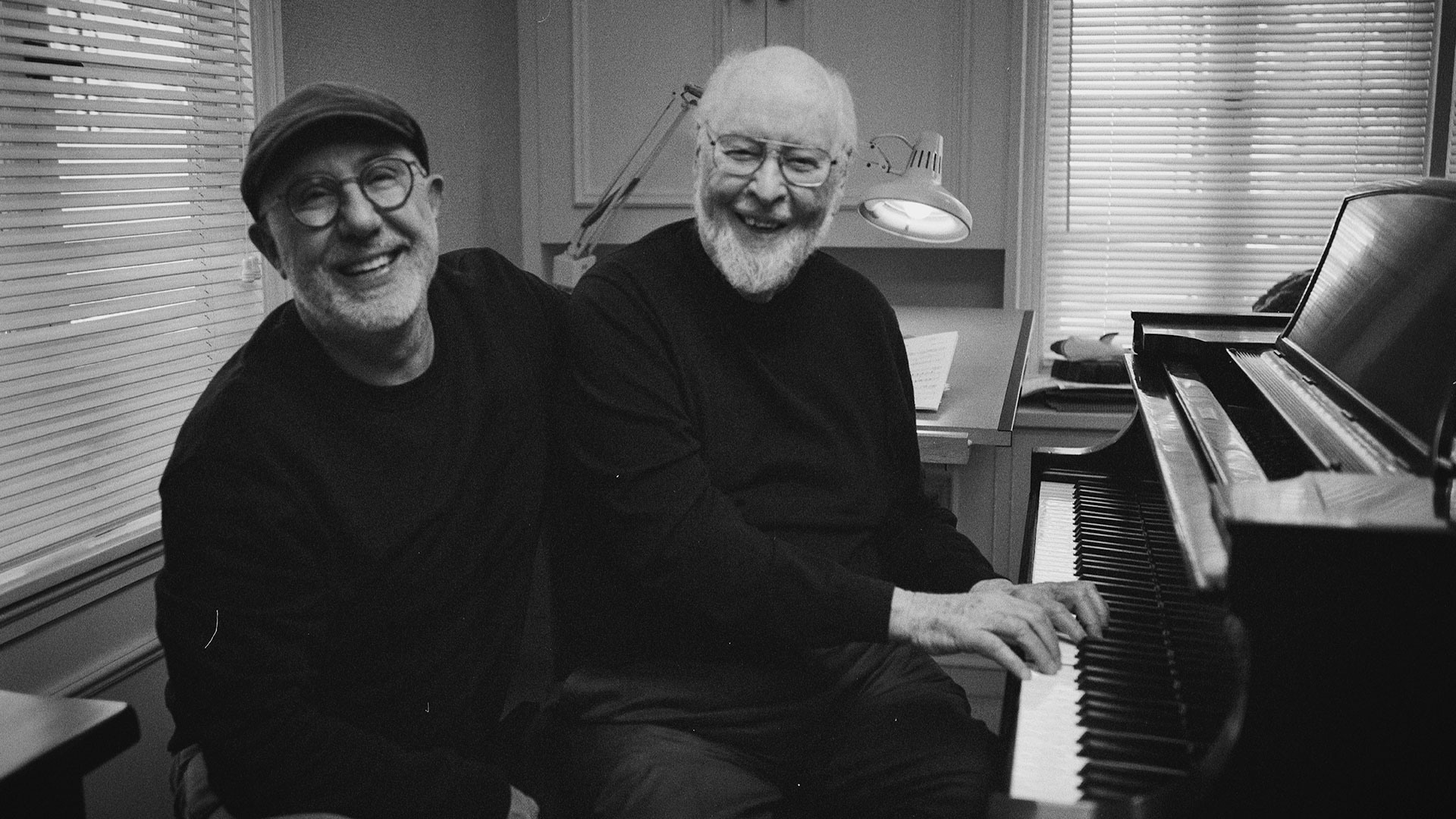 Director Laurent Bouzereau and composer John Williams smile at the piano together.