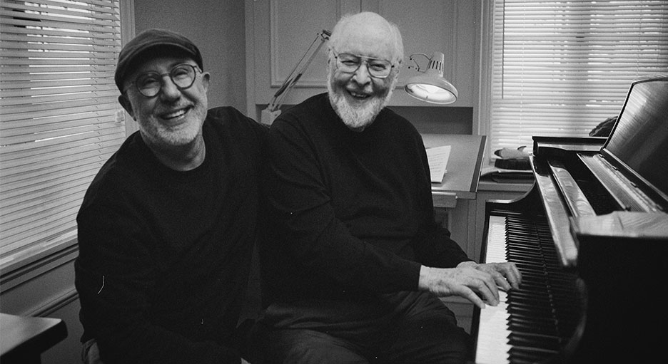 Director Laurent Bouzereau and composer John Williams smile at the piano together.