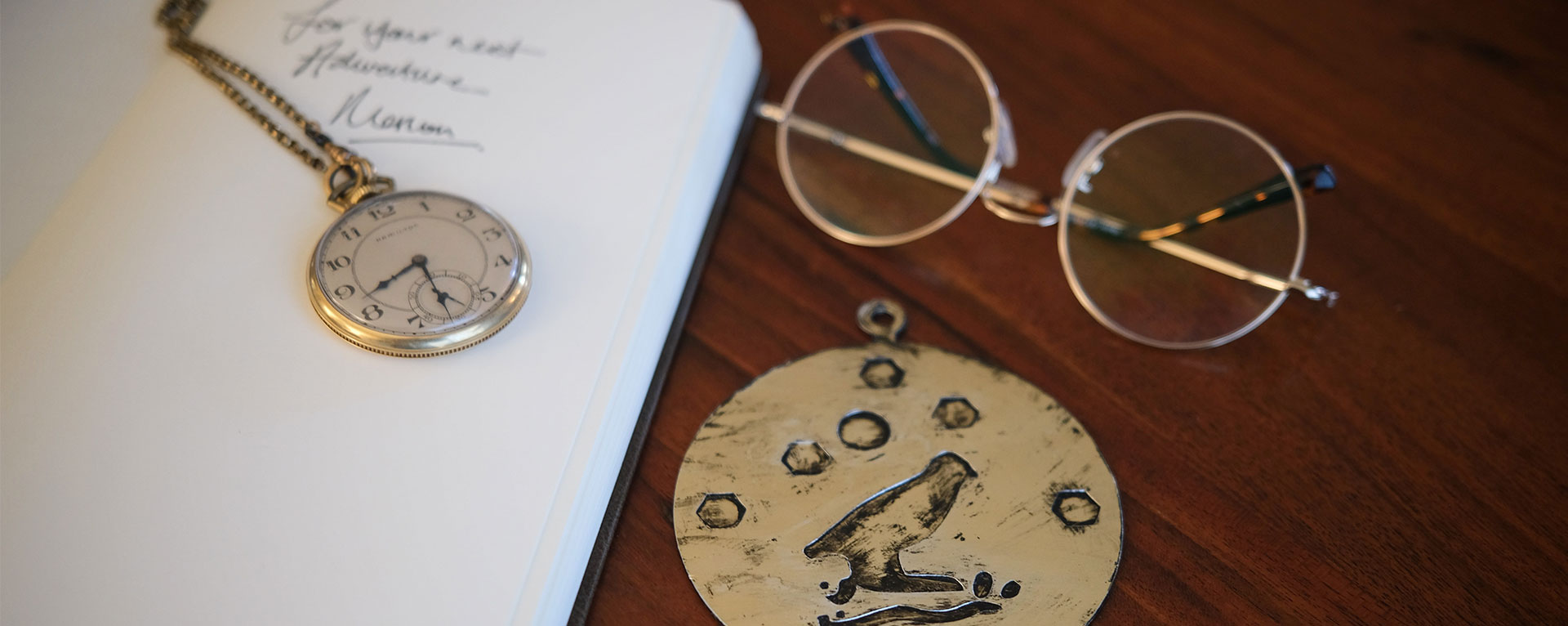 The medallion on a desk with a journal, watch, and glasses.