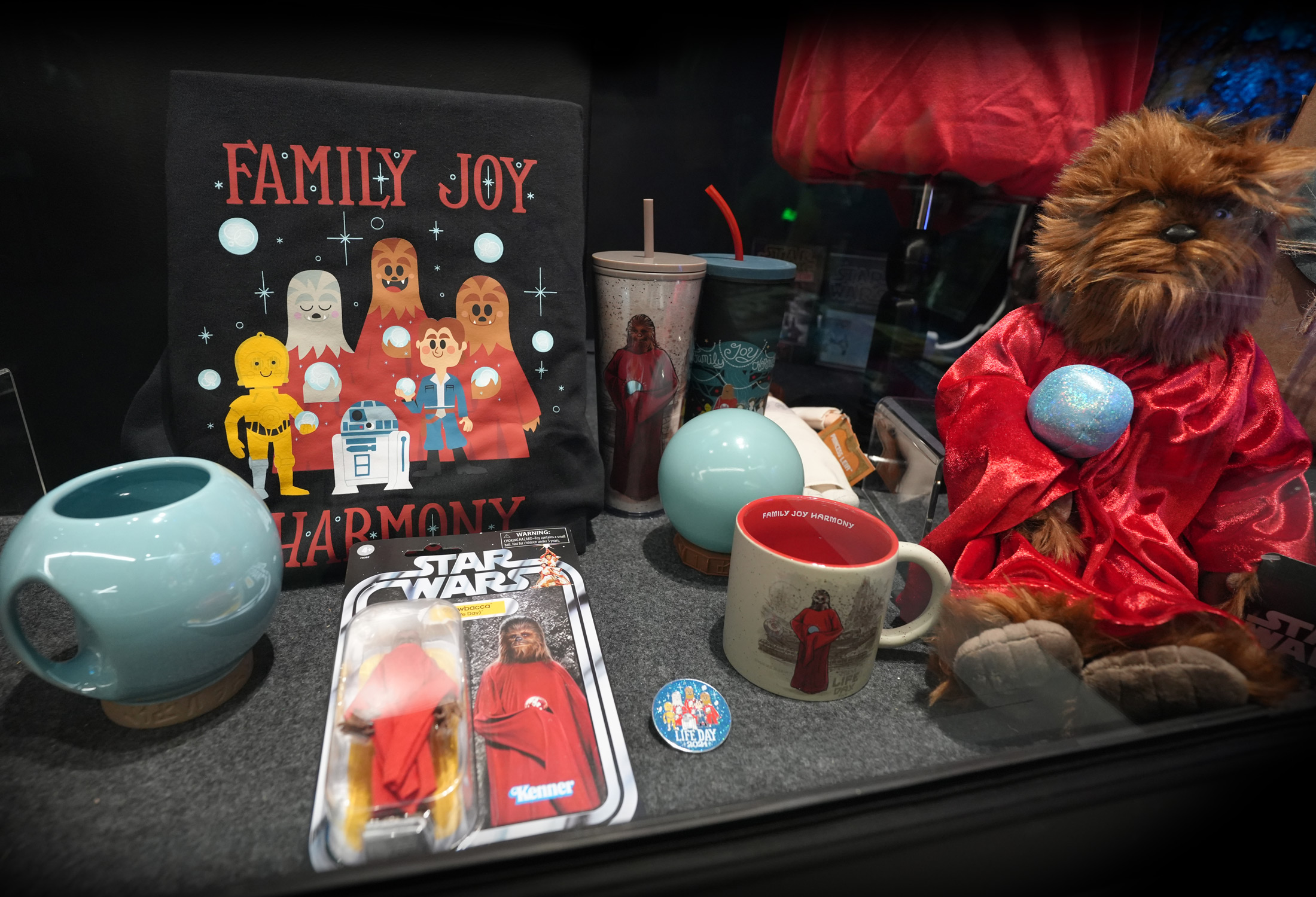 On display throughout the exhibit are several items inspired by Life Day-inspired items from previous years, which were available at Disney Parks starting in 2021, with most offered only during a given year. Featured here are a large plush Chewbacca, an illuminated Life Day orb and ceramic mug, tumblers, a Chewbacca Life Day action figure and more, including a new adult pullover hoodie and pin for 2024.